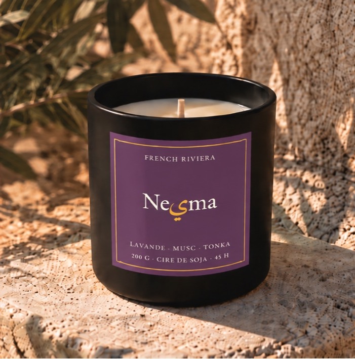 Nesma Lavande et Musc candle in matte black glass with its plum label, on sunlit stone.