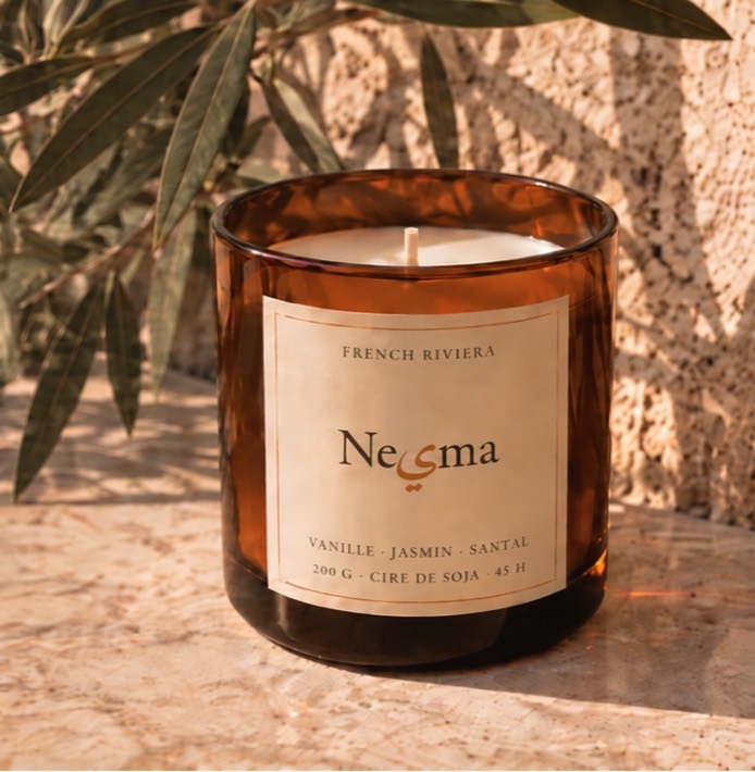 Nesma Vanille candle in amber glass with its cream label, on sunlit stone.